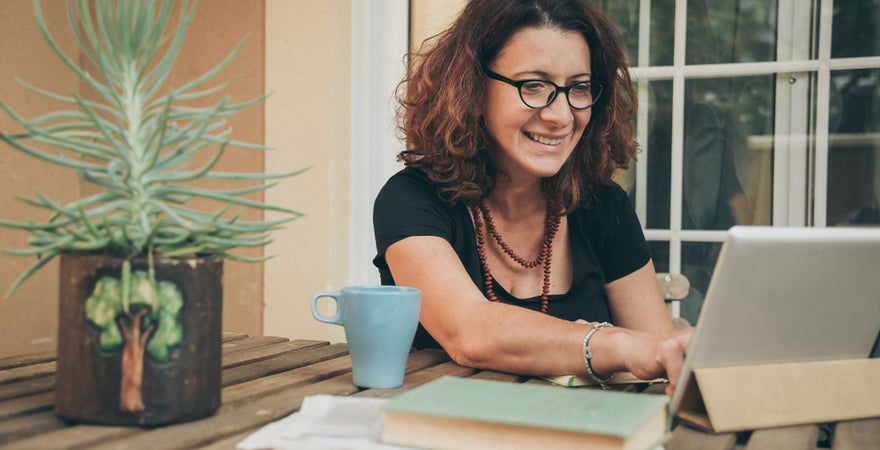 An ECU Online student sits outside at a table organising her time management with with a tablet and books.