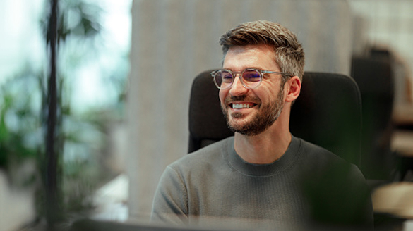 A smiling man with glasses sits in an office, surrounded by a professional environment.