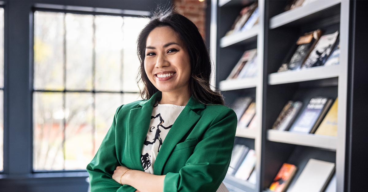 Woman in green blazer standing in front of bookshelves.
