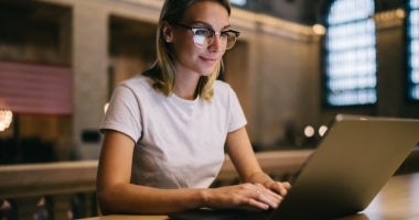 An ECU Online Education student sits by a window working on her laptop.