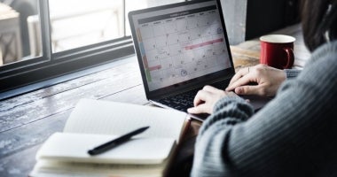 An ECU Online Student is sitting at a desk. We can see their notebook and laptop screen which has a weekly planner open.